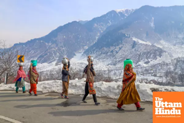 Ganderbal: Women carry water containers on their heads while walking along a snow-covered road