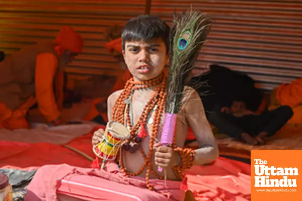 Prayagraj: A child with Pellet drum (Damru) and Peacock feather poses for a photo at the Triveni Sangam